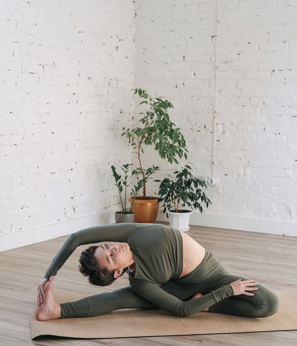 Woman performing a gentle back-stretching yoga pose in a calm, green-tinted room.